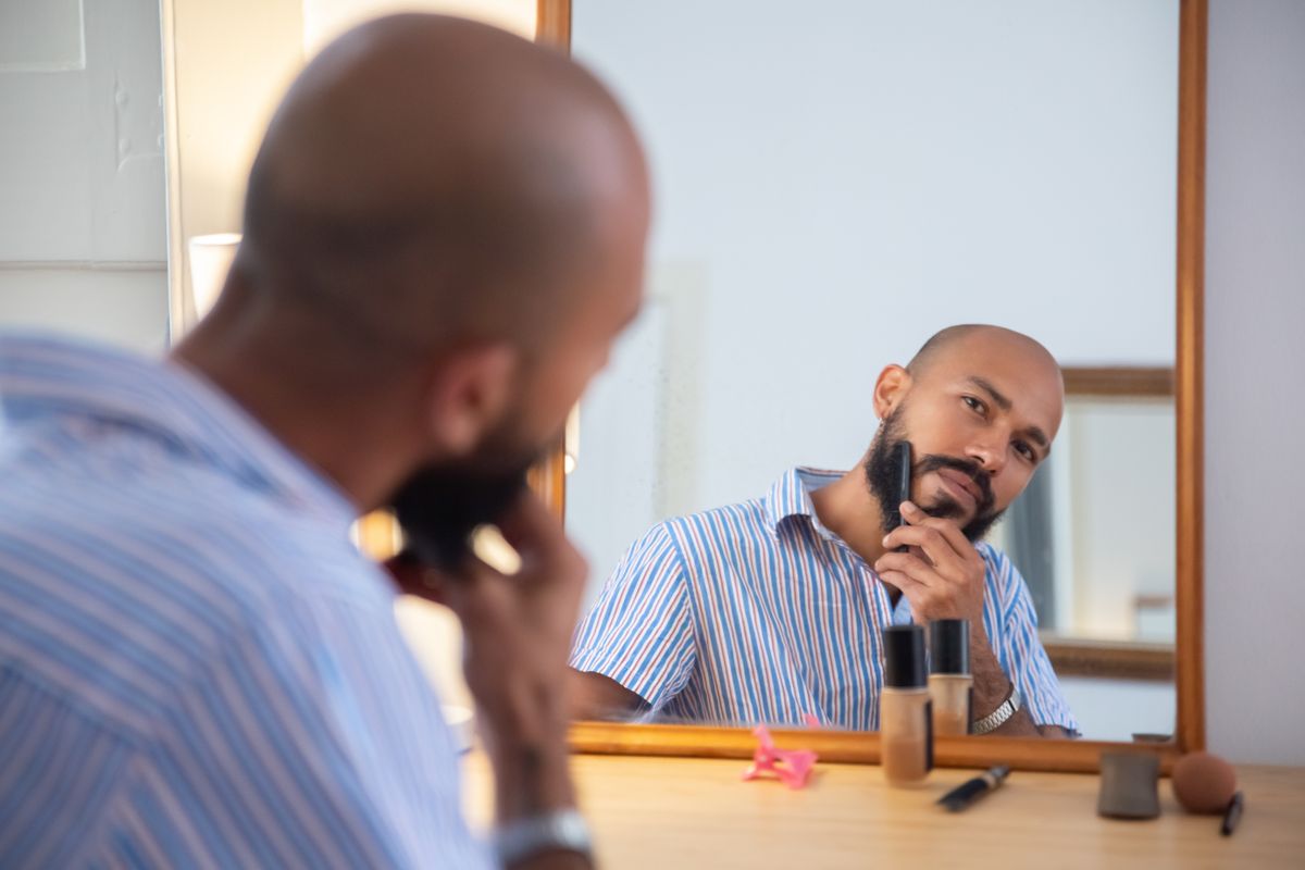 Man combing and checking his beard in front of a mirror