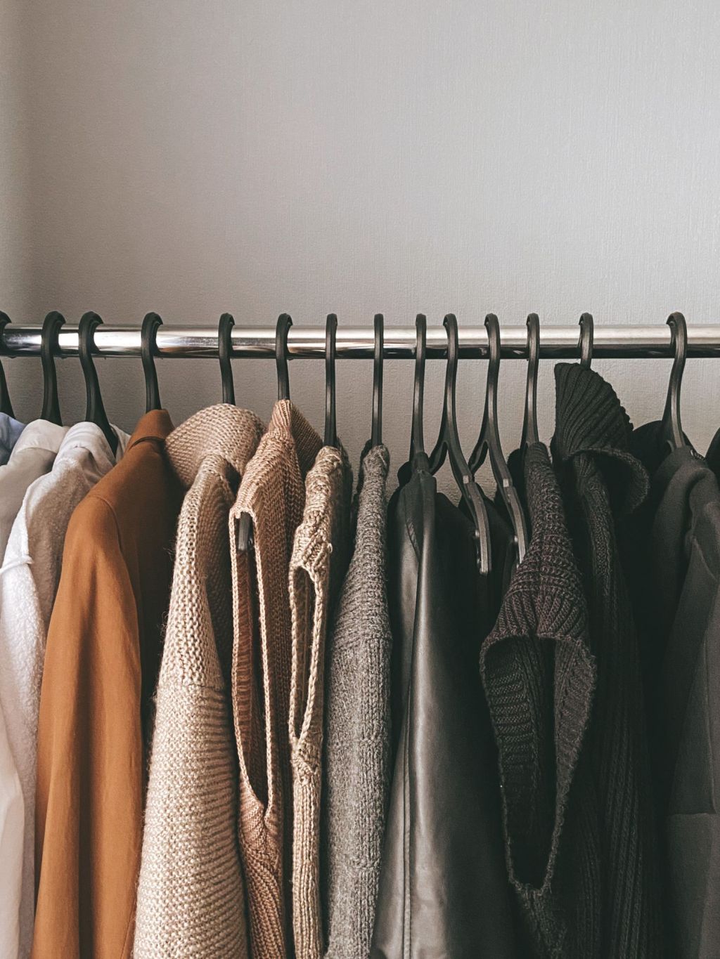 Collection of knit sweaters in understated colours hanging neatly on a clothes rail