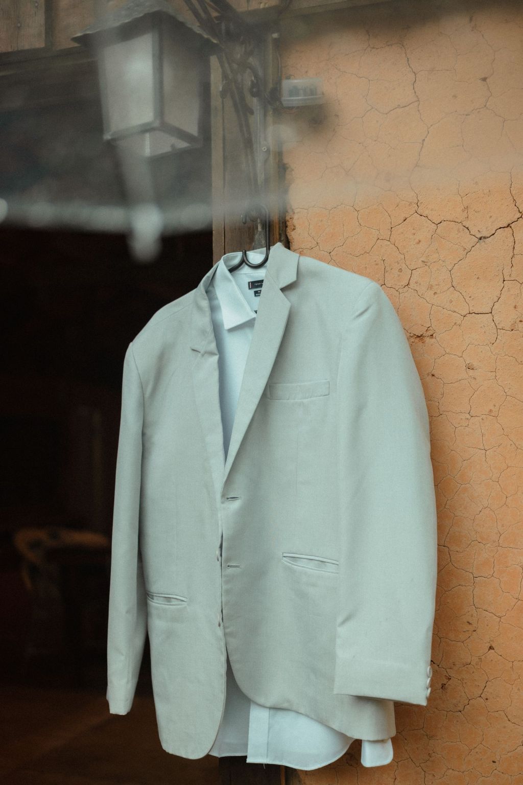 A classic beige suit jacket hanging against a rustic neutral wall with no visible brand logo